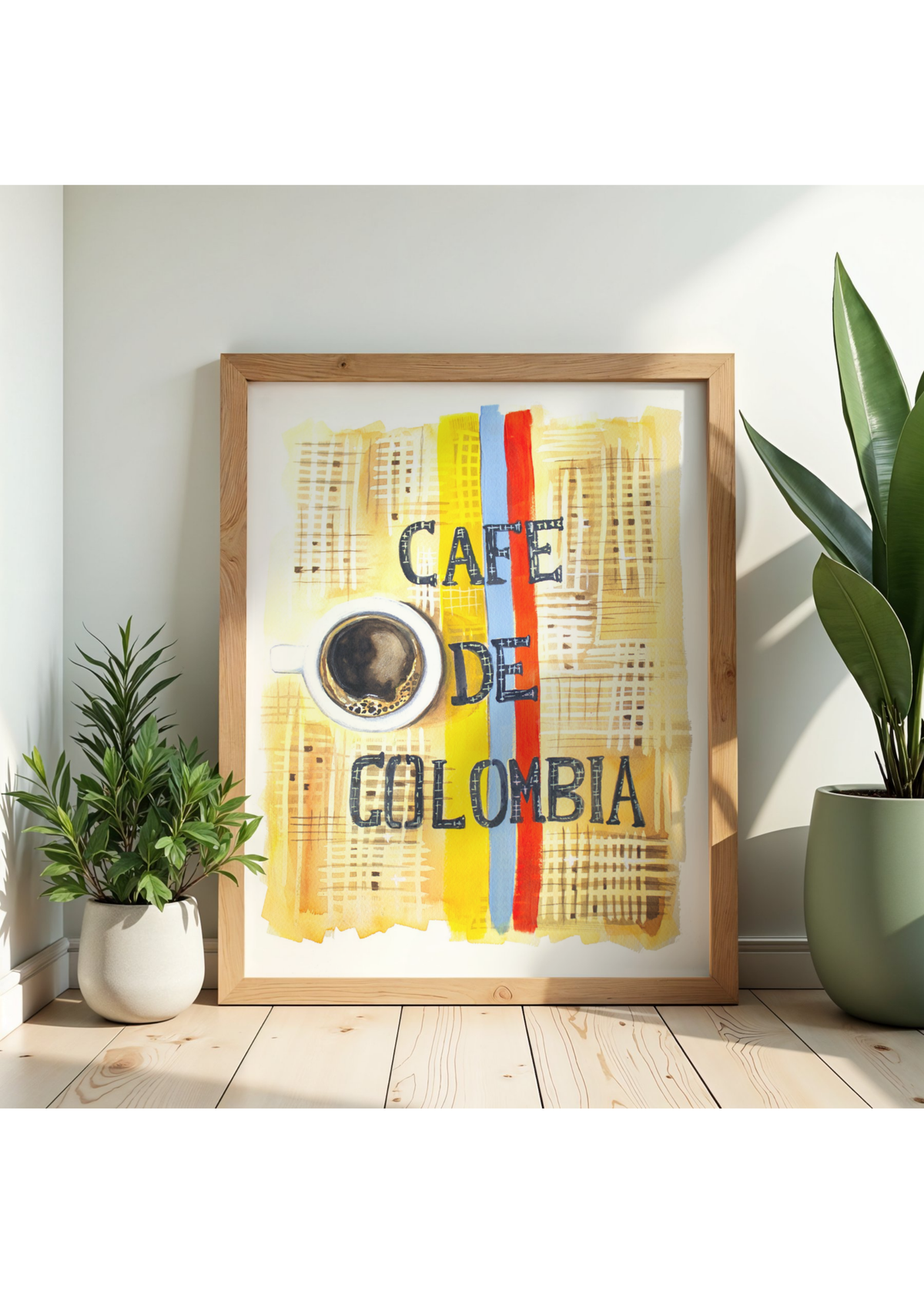 A framed art print featuring a stylized yellow coffee cup and the words 'CAFE DE COLOMBIA' with vertical red, yellow, and blue stripes, displayed on a light wood floor against a white wall with potted plants.