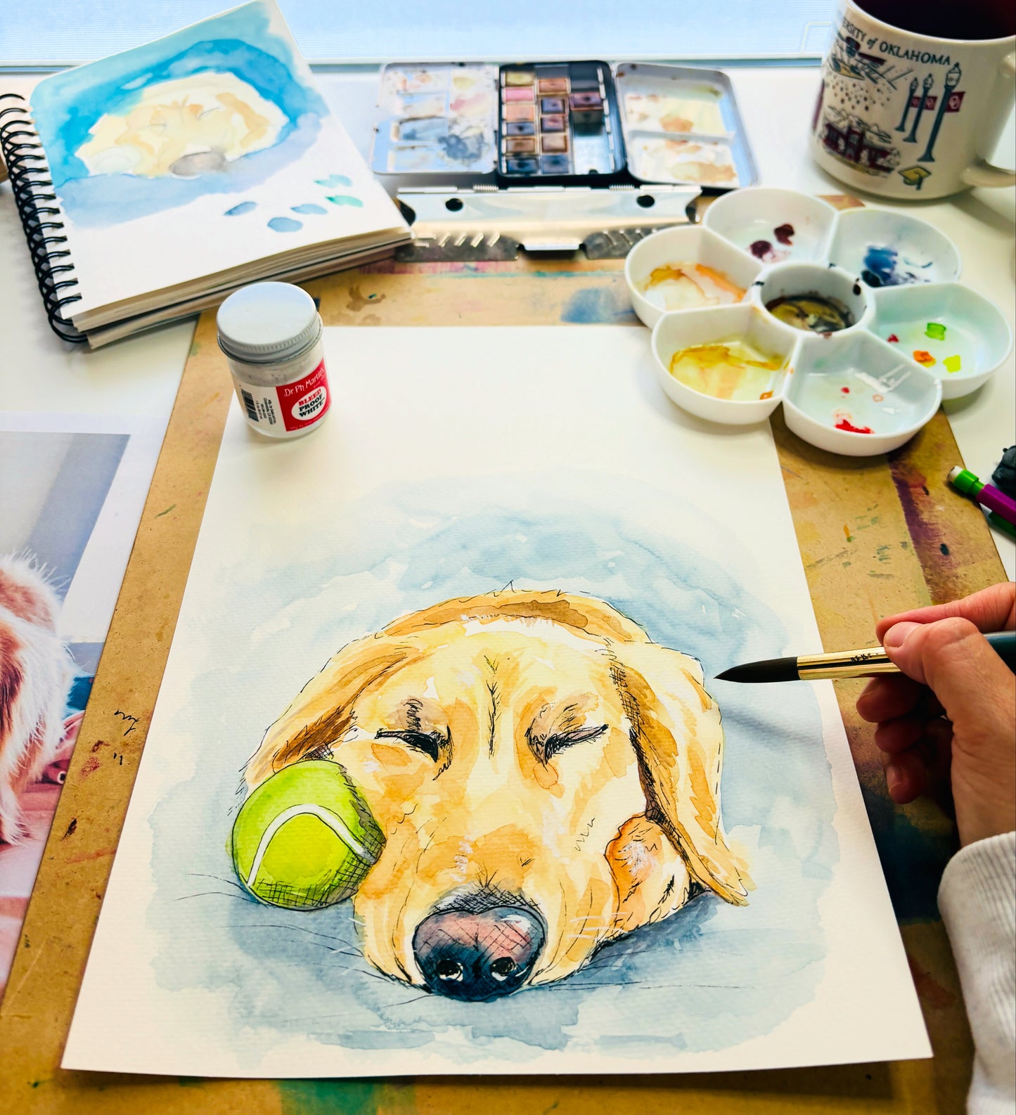 Artistic depiction of a dog with a tennis ball, surrounded by art supplies on a table.