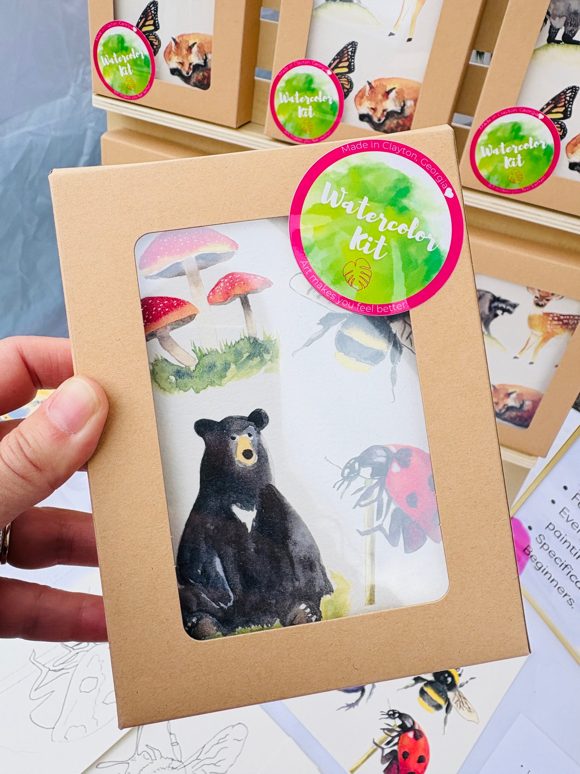 Watercolor kit packaging with a bear illustration held by a hand.
