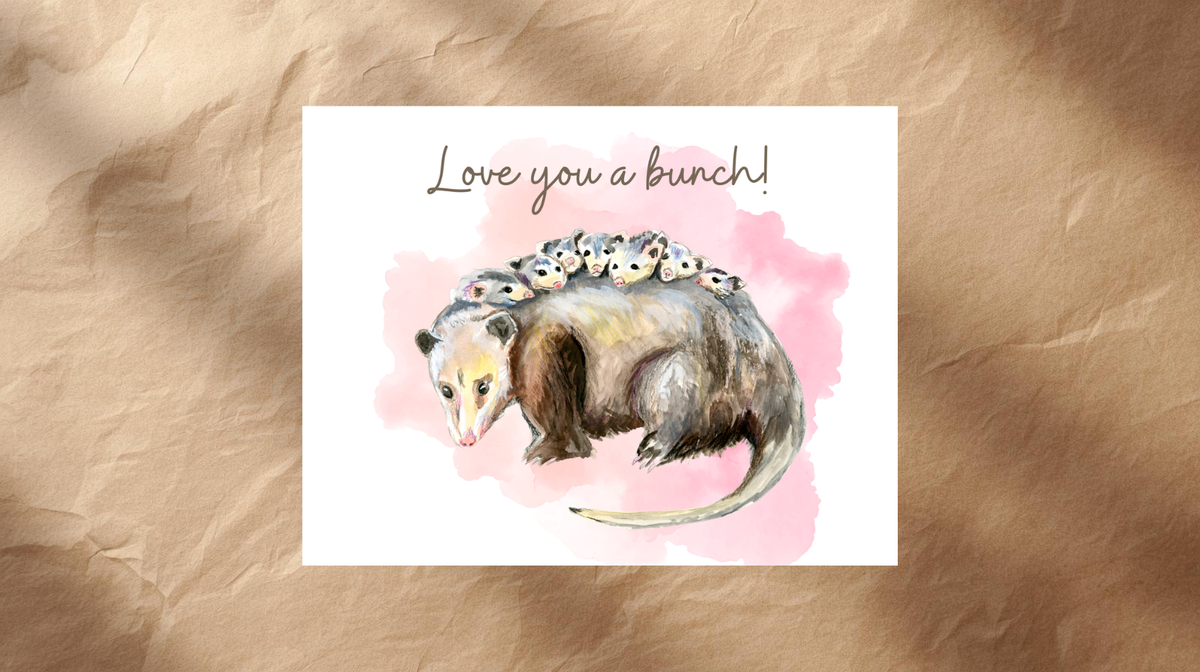 A square greeting card featuring a watercolor illustration of a small mammal with several baby animals on its back, with the handwritten text 'Love you a bunch!' above. The card is centered on a textured brown paper background.